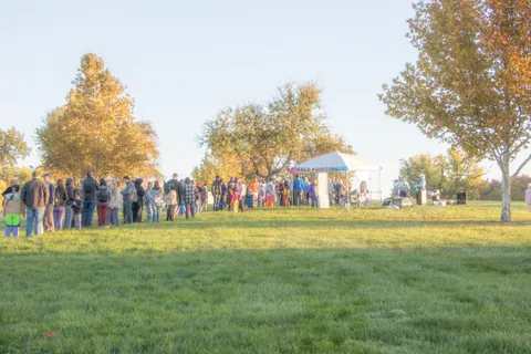 A crowd gathers in a golden-lit field near a small gazebo and tent.