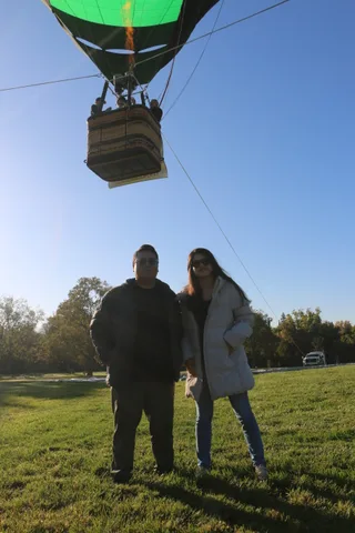 A couple stands on the grass watching the basket rise into the sky.