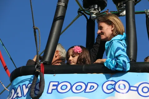 A small group including a girl with a flower headband rides together in the basket.