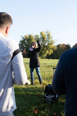 A person seen from behind raises a megaphone in a blurred motion shot across the grass.