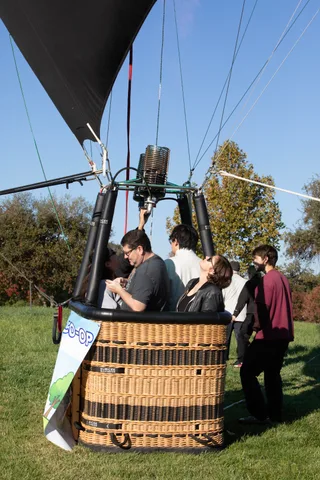A group gathers around the basket on the grass with event tents visible behind them.