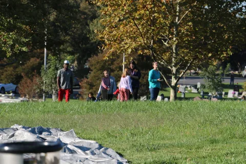 A small crowd gathers on the open grass near trees at the balloon launch field.