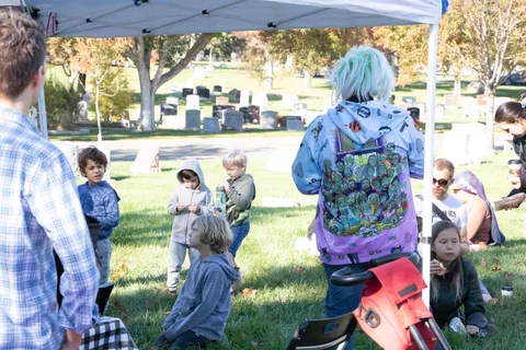 A child in a tie-dye zombie costume walks with others near an event tent.