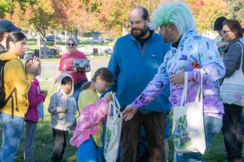 A costumed volunteer hands out tote bags to a colorful group that includes several kids.