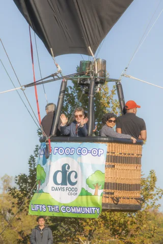 The full Davis Food Co-op 'Lifts the Community' banner wraps the basket with riders barely visible above.