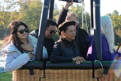 Riders wave and smile from the basket as the balloon rises.