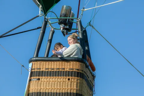 An adult and child ride in the basket with the burner and rigging visible above them.