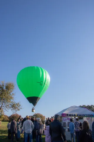 A full green hot air balloon hovers over a crowd gathered near the face painting tent.