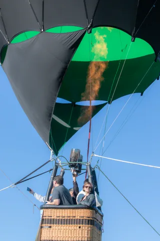 A man and a woman stand together in the basket against open sky.