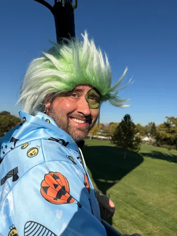 A close portrait of a man smiling in a green wig and eye patch costume.
