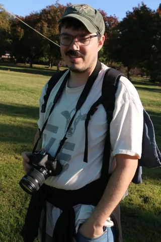 A man with a camera around his neck stands on the grass at the balloon launch.