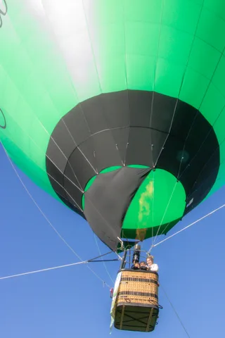 The green striped balloon dominates the frame with the tiny basket hanging far below.