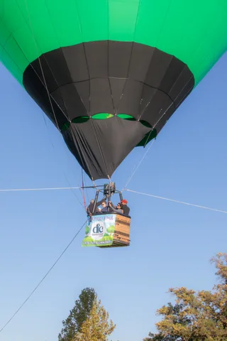 The balloon climbs small against a huge expanse of blue sky.