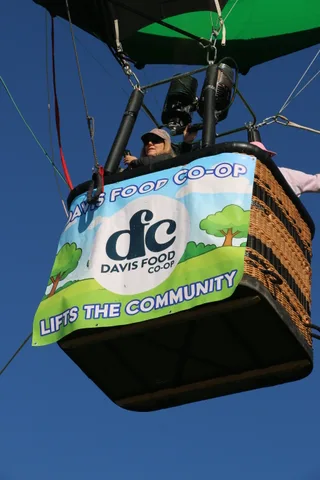 Riders in the balloon basket are partly washed out by sun glare above the banner.