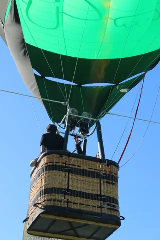 The green balloon envelope dominates the frame with its basket small at the bottom.
