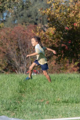 A girl runs across the grass with arms out, caught mid-stride in warm light.