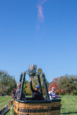Two people stand in the basket during setup with autumn trees behind them.