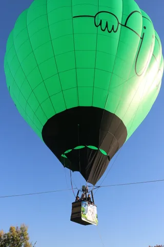 The green balloon fabric with its drawn logo fills the frame against the sky.