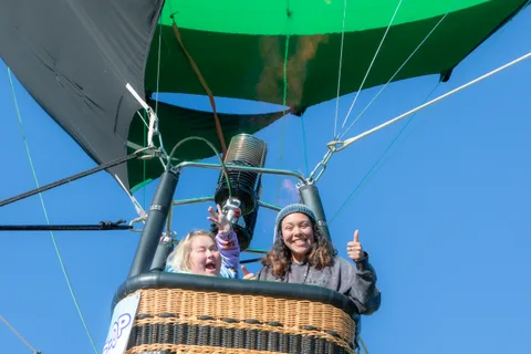 A delighted girl peers out of the basket next to a woman giving a thumbs up under the green envelope.