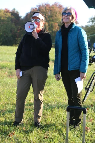An emcee speaks into a megaphone next to a companion on the grass.