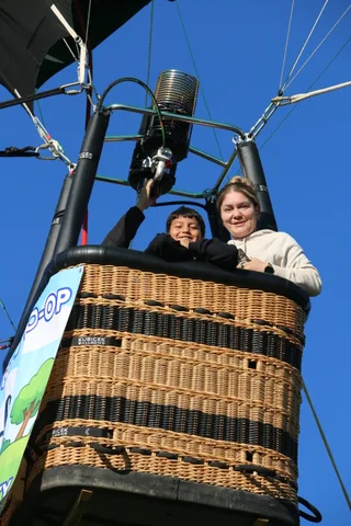 Two children peer over the basket rim against the blue sky.