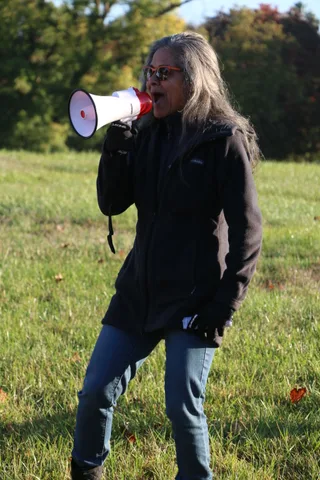 A woman with gray hair and sunglasses speaks into a megaphone.