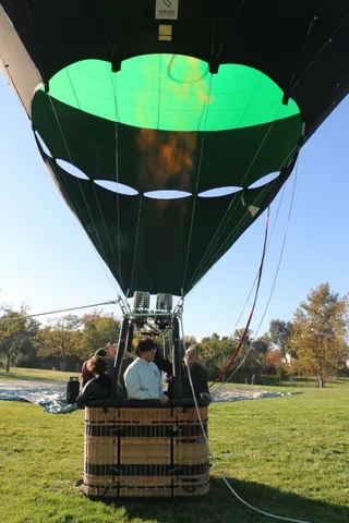 The burner fires into the balloon envelope as riders watch from the basket.
