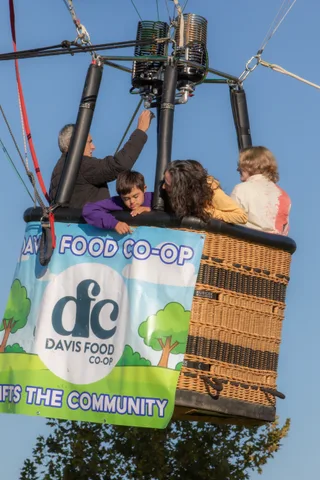 The full Davis Food Co-op 'Lifts the Community' banner wraps the basket, riders barely visible above.