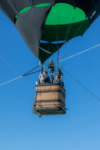 Three riders float in the basket high above the open sky.