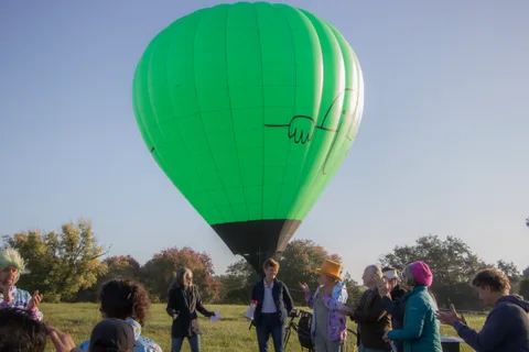 The green balloon rises into the sky as a small group watches from below.
