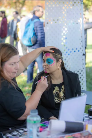A volunteer paints blue and pink face paint on a woman's forehead at the festival.