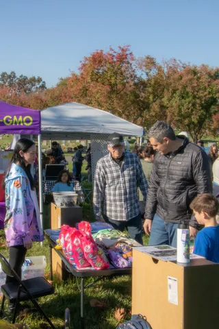 A volunteer in a purple jacket chats with guests at a cemetery booth.
