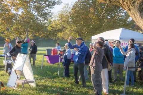 People gather near tents and a folding sign at the event staging area.