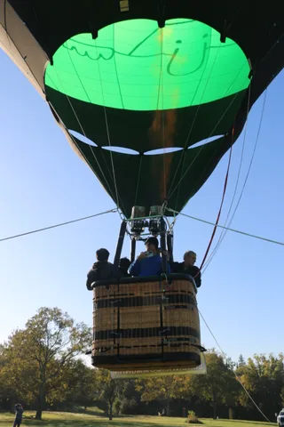 The balloon basket rises with a lone figure watching from the field below.