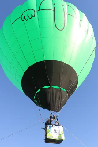 A green and black hot air balloon floats high in a clear blue sky with its basket below.