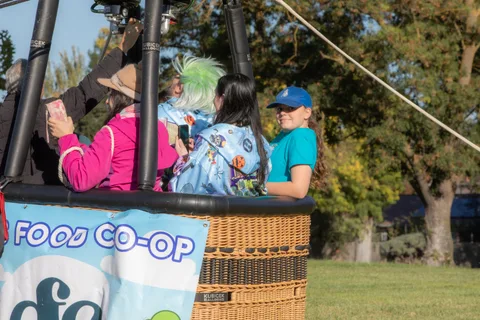 Riders in the balloon basket raise a hand in greeting, cropped close.