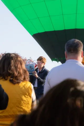 The balloon's canopy edges into frame above a small crowd gathered by a sign.