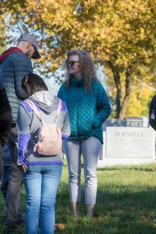 Two women stand together near a headstone in the cemetery, seen from the side.