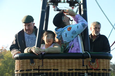 A man reaches to help a costumed rider adjust their hood in the basket.