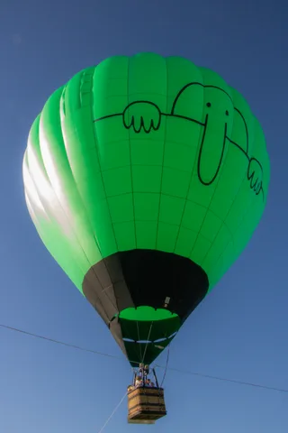 A playful doodled face is painted onto the green balloon fabric against the sky.