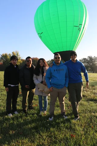 A different group of five poses together on the lawn as the balloon looms behind them.