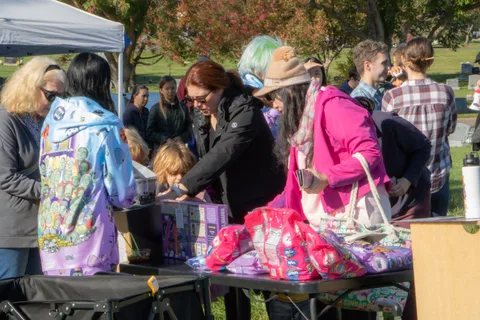 A group of festival guests gather and chat around a giveaway table.