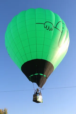 The balloon rises with its basket visible against the sky.