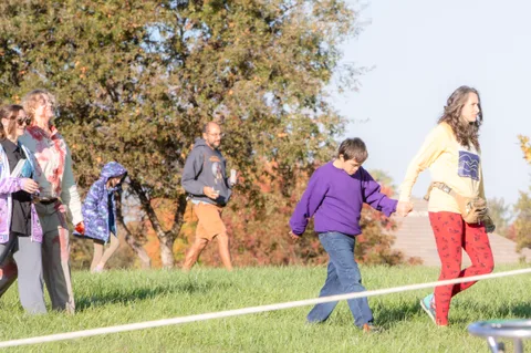 A loose group of families and kids plays on the grass near a tent.