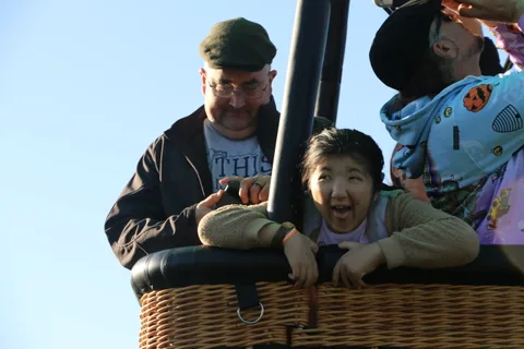 A girl grins with delight in the balloon basket as her dad looks on.