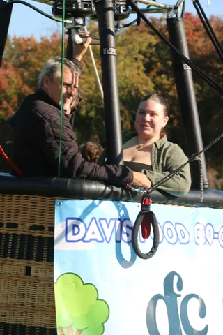 A group in dark jackets stands in the balloon basket, mostly turned away.