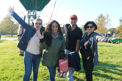 Four friends wave and laugh together as the balloon towers behind them.