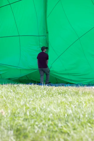 A person drapes green balloon fabric across the grass, legs visible above.