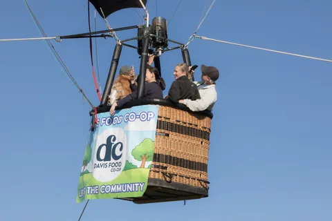 Three riders stand together in the basket beneath crossing rigging lines.
