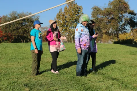 Three people chat together on the open grass near the balloon launch field.